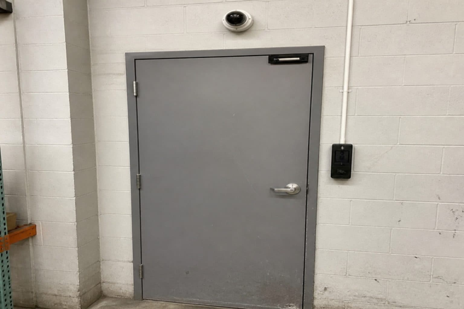Illustration: a steel warehouse door with a magnetic lock, an access-control reader on the wall beside the handle and a dome camera above