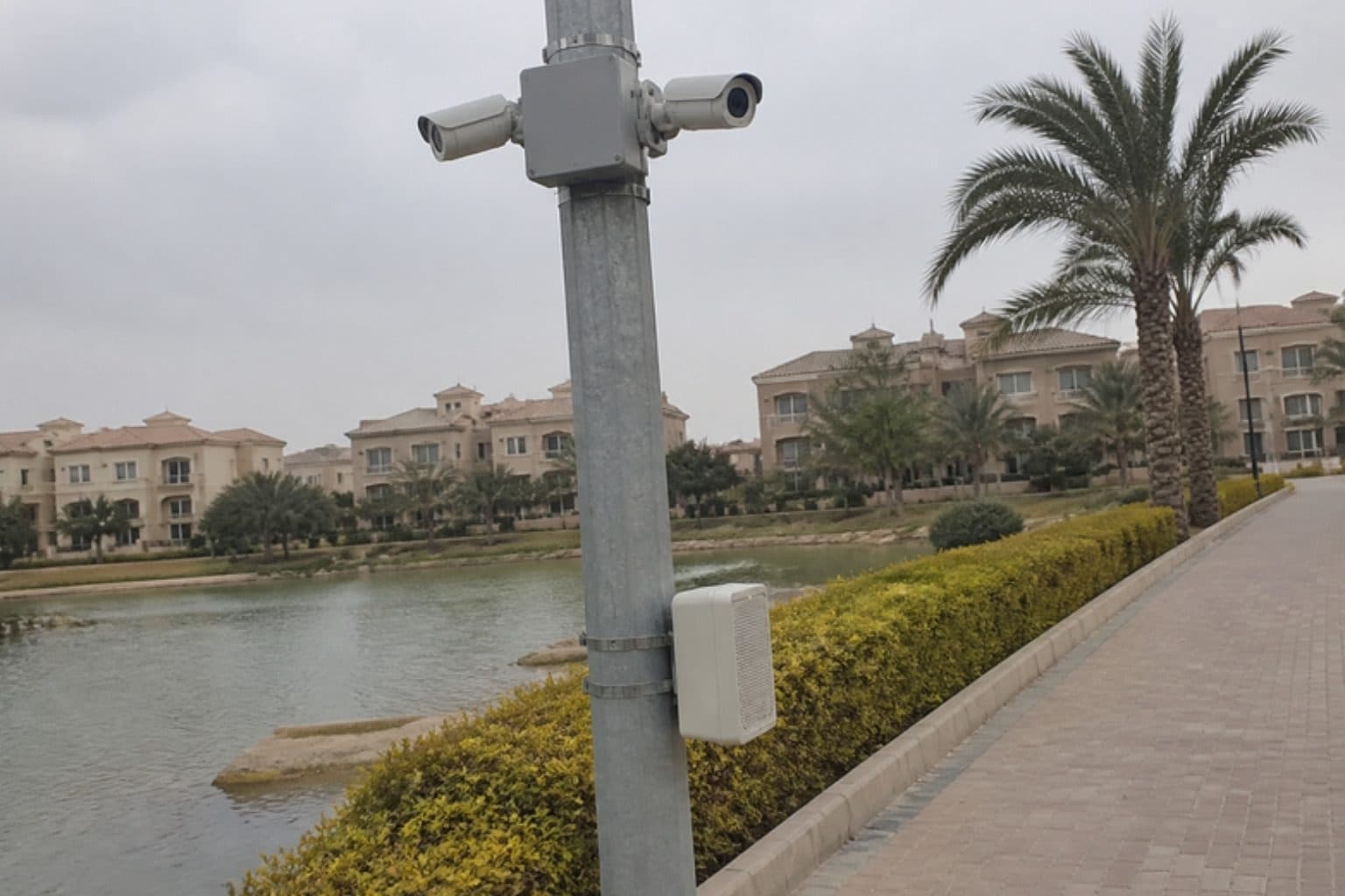 Illustration: a pole beside a lakeside walkway with two cameras facing opposite ways and an outdoor speaker