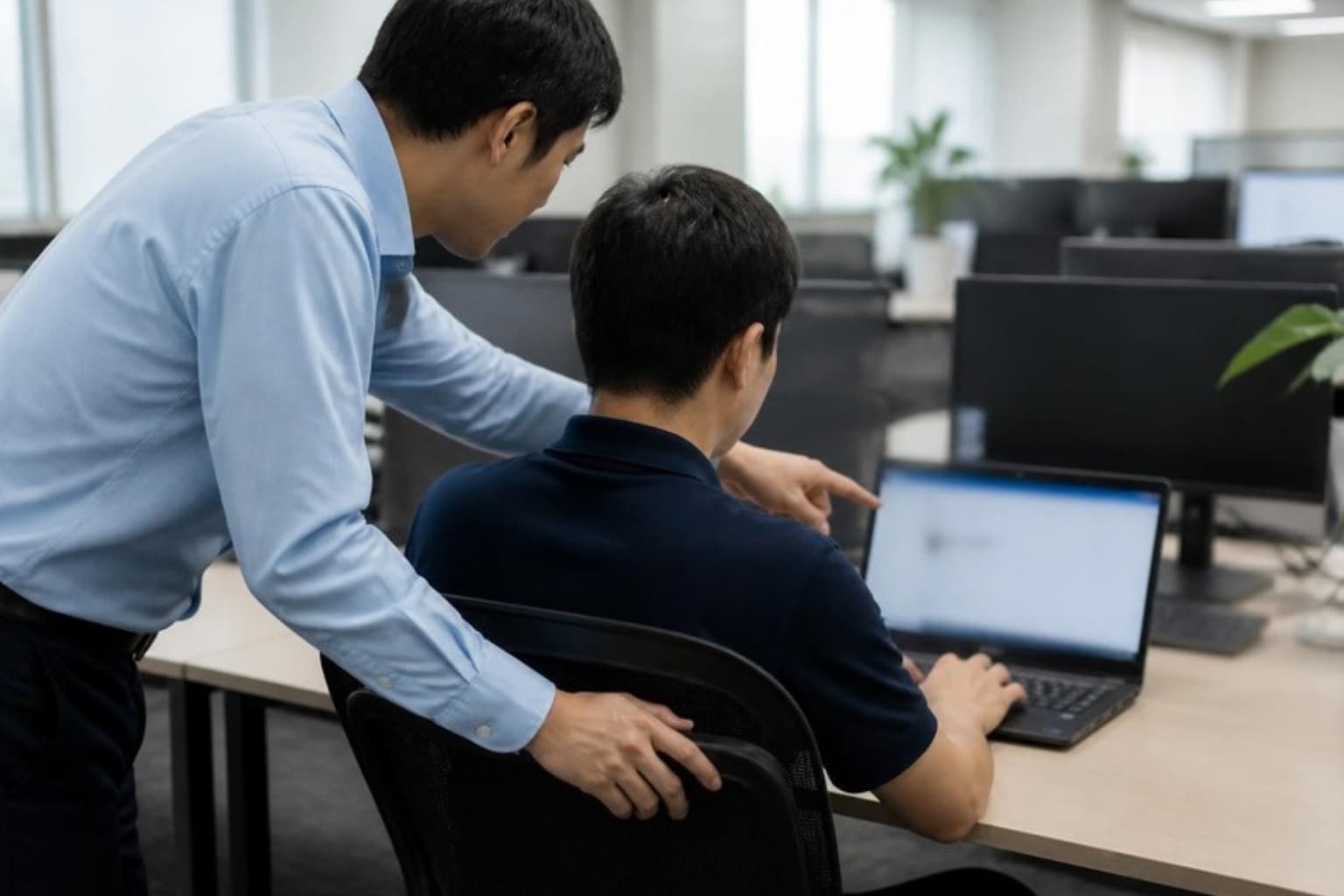 An engineer pointing at an employee's laptop screen while helping at their desk